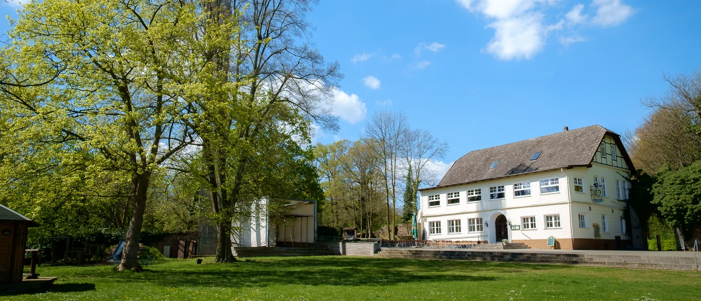 El Castillo Ein weißes Gebäude mit Satteldach steht neben einem hohen Turm, umgeben von grünen Bäumen.