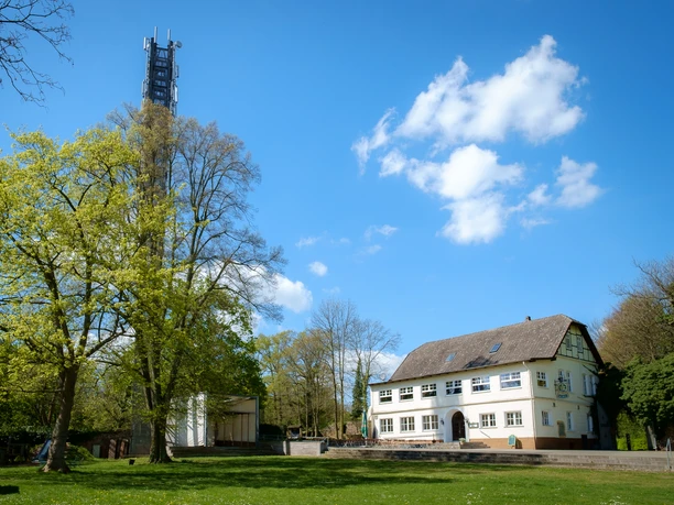 El Castillo Ein weißes Gebäude mit Satteldach steht neben einem hohen Turm, umgeben von grünen Bäumen.