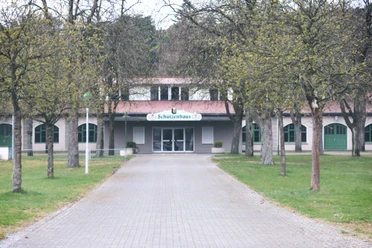 IMG_0501.JPG Breit angelegter, gepflasterter Weg führt zum historischen Schützenhaus, umgeben von laubfreien Bäumen.