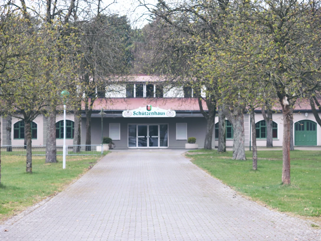 IMG_0501.JPG Breit angelegter, gepflasterter Weg führt zum historischen Schützenhaus, umgeben von laubfreien Bäumen.