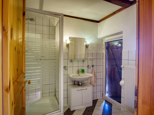 bad.jpg Helles Badezimmer mit Duschkabine, Waschbecken, Spiegel, weißen Fliesen und Holztür.