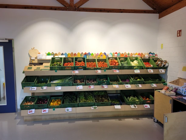 Ein Verkaufsregal in einem Hofladen bietet frisches, regionales Gemüse in grünen Kisten an.