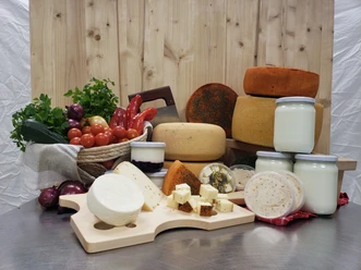 Hofladen Produkte Regionale Produkte: Käselaibe, Käsewürfel, Milchgläser und frisches Gemüse auf einem Holzbrett.