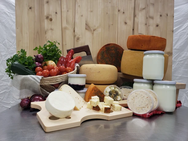 Hofladen Produkte Regionale Produkte: Käselaibe, Käsewürfel, Milchgläser und frisches Gemüse auf einem Holzbrett.
