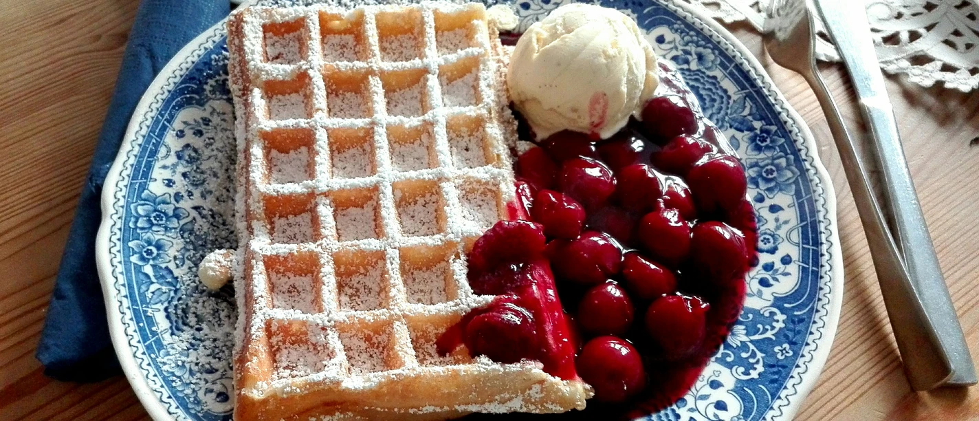 Waffeln mit Kirschen und Eis Waffel mit Puderzucker, Kirschen und Vanilleeis auf blauem Porzellanteller, auf Holzuntergrund.