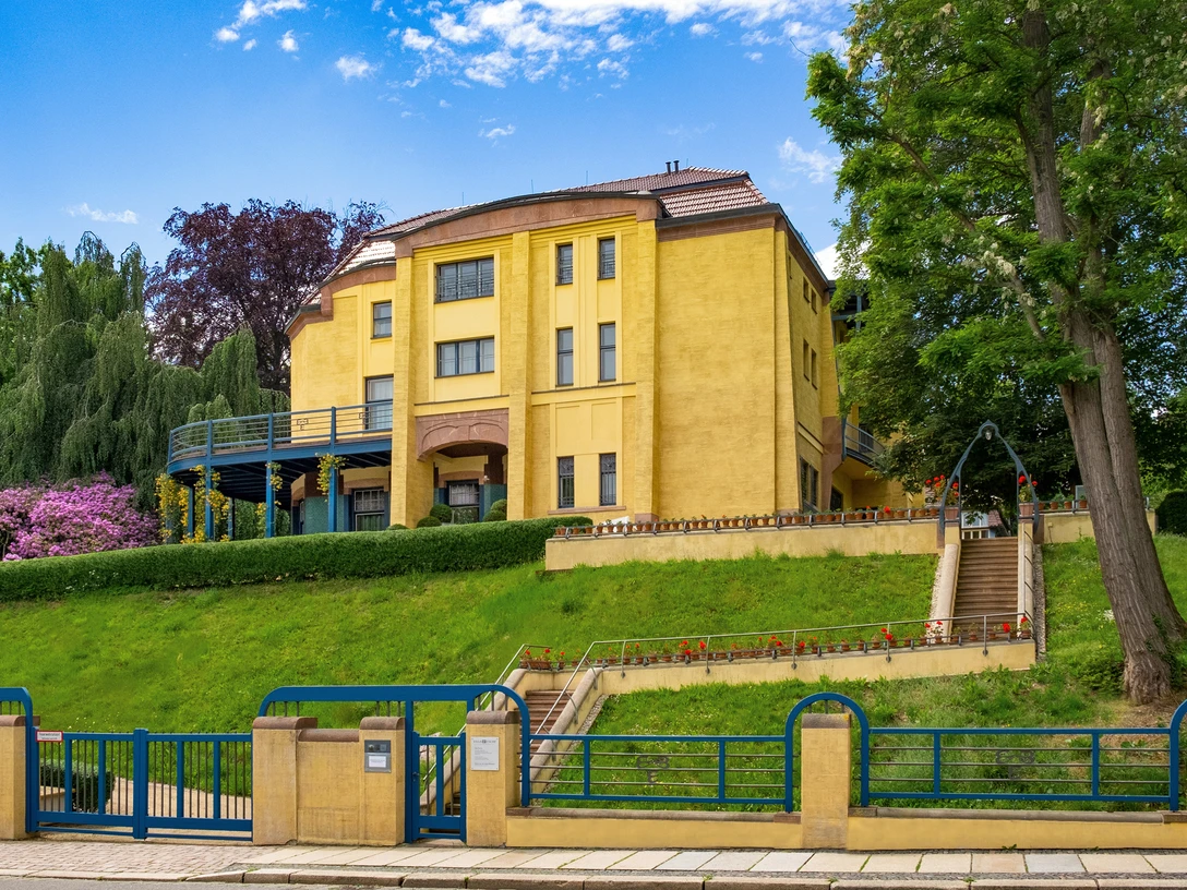 KSC-Villa Esche-Foto-FrankKrueger-entsättigt-m.jpg Historische Villa mit gelber Fassade und Treppenzugang, umgeben von Garten und Bäumen.Historic villa with yellow façade and staircase access, surrounded by garden and trees.Historická vila se žlutou fasádou a přístupem po schodišti, obklopená zahradou a stromy.Zabytkowa willa z żółtą fasadą i wejściem po schodach, otoczona ogrodem i drzewami.Historische villa met gele gevel en toegang via trappenhuis, omgeven door tuin en bomen.Villa storica con facciata gialla e scala di accesso, circondata da giardino e alberi.