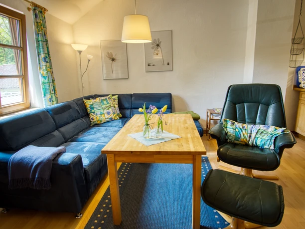 Wohnzimmer Wohnzimmer mit blauem Ecksofa, Holztisch auf blauem Teppich und dunklem Ledersessel.