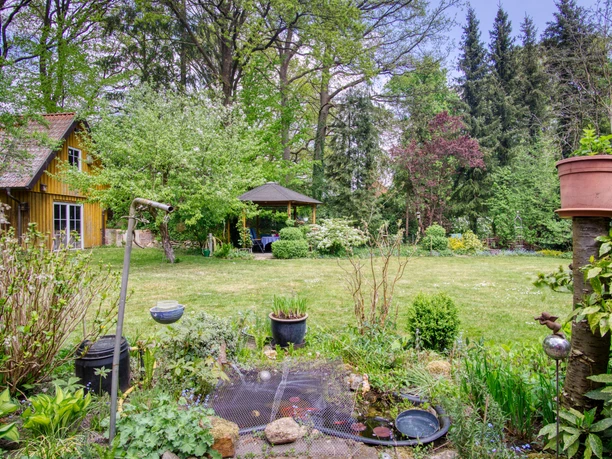 Garten Grüner Garten mit kleinem Teich, einem gelben Holzhaus und einem Pavillon zwischen Bäumen.