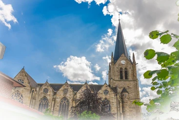 Kath. Kirche St. Benedikt Lengerich, Quelle Karin Knus.jpg Neugotische St.-Benedikt-Kirche in Lengerich mit hohem Turm und Uhr vor blauem Himmel mit Wolken.