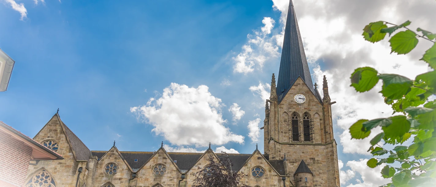 Kath. Kirche St. Benedikt Lengerich, Quelle Karin Knus.jpg Neugotische St.-Benedikt-Kirche in Lengerich mit hohem Turm und Uhr vor blauem Himmel mit Wolken.