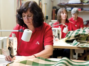 Näherin Strandkorbherstellung Eine Näherin näht konzentriert an einem grünen, gestreiften Stoff in einer Werkstatt zur Strandkorbherstellung.