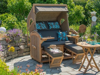 Strandkorb im Ausstellungsgelände Ein Strandkorb steht auf einer sonnigen Terrasse, umgeben von blühendem Grün, bereit zum Entspannen.