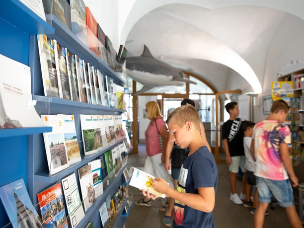Foyer Junge blättert in Broschüre, umgeben von weiteren Besuchern im modernen Foyer.