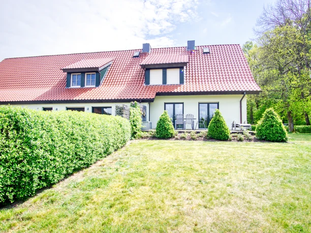 außen-hinten-whg-2.jpeg Rückseite eines weißen Ferienhauses mit rotem Dach, möblierter Terrasse und Rasenfläche.