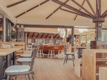 Eine mit Holzböden versehene Terrasse mit Stühlen und Tischgruppen unter einer großen Überdachung.