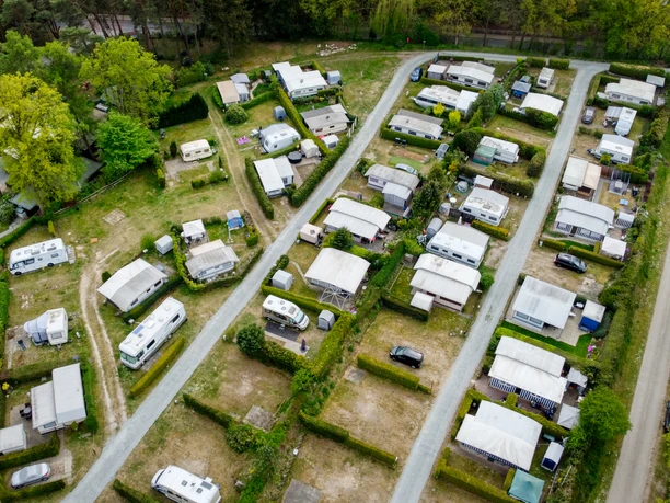 Campingplatz Lopautal Luftaufnahme eines gepflegten Campingplatzes mit Wohnwagen und Mobilheimen in grüner Umgebung. Schmale Wege führen zwischen den Parzellen hindurch, umgeben von Hecken und Bäumen. Der Platz wirkt geordnet und ruhig, eingebettet in eine von Wäldern und Wiesen geprägte Landschaft des Lopautals.