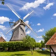 Eine historische Windmühle mit großen Flügeln, umgeben von traditionellen Gebäuden und Bäumen.