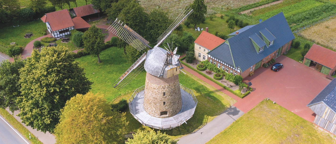Eilhauser Königsmühle Historische Windmühle mit Steinstruktur und großen Flügeln, umgeben von grünen Feldern und Gebäuden.