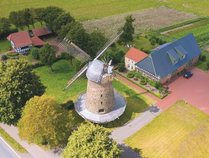 Eilhauser Königsmühle Historische Windmühle mit Steinstruktur und großen Flügeln, umgeben von grünen Feldern und Gebäuden.