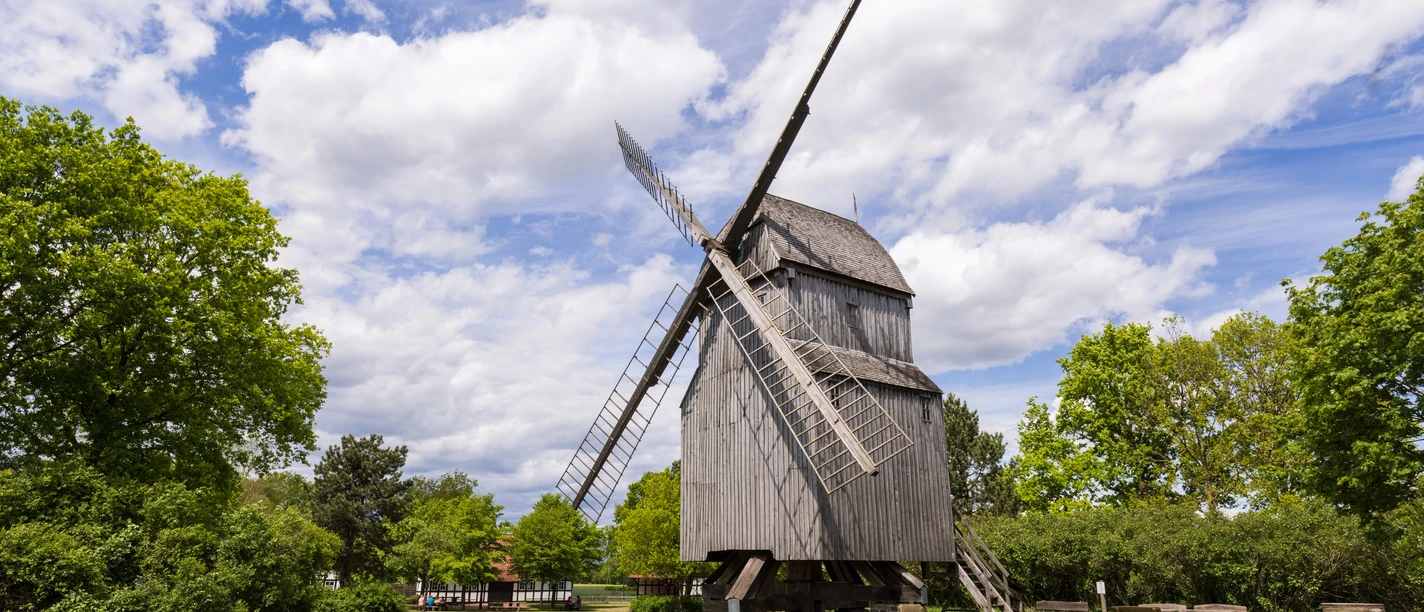 Bockwindmühle Oppenwehe Die historische Bockwindmühle Oppenwehe steht an grüner Wiese, umgeben von Bäumen und blauem Himmel.