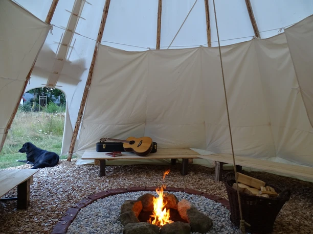 Lagerfeuer im Tipi Campfire in the tepee, a guitar on the bench, fiery ambience, a dog resting outside.