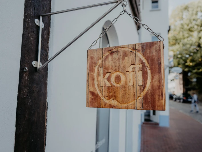 Minden - kofi-79.jpg Das Bild zeigt ein Holzbrett mit dem Geschäftsnamen.