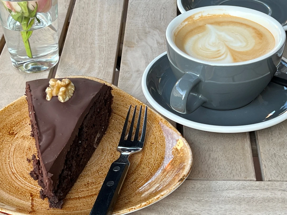 Schokokuchen Ein Stück gläserner Schokokuchen mit Walnuss auf einem Teller neben einem Cappuccino mit Herzmuster.