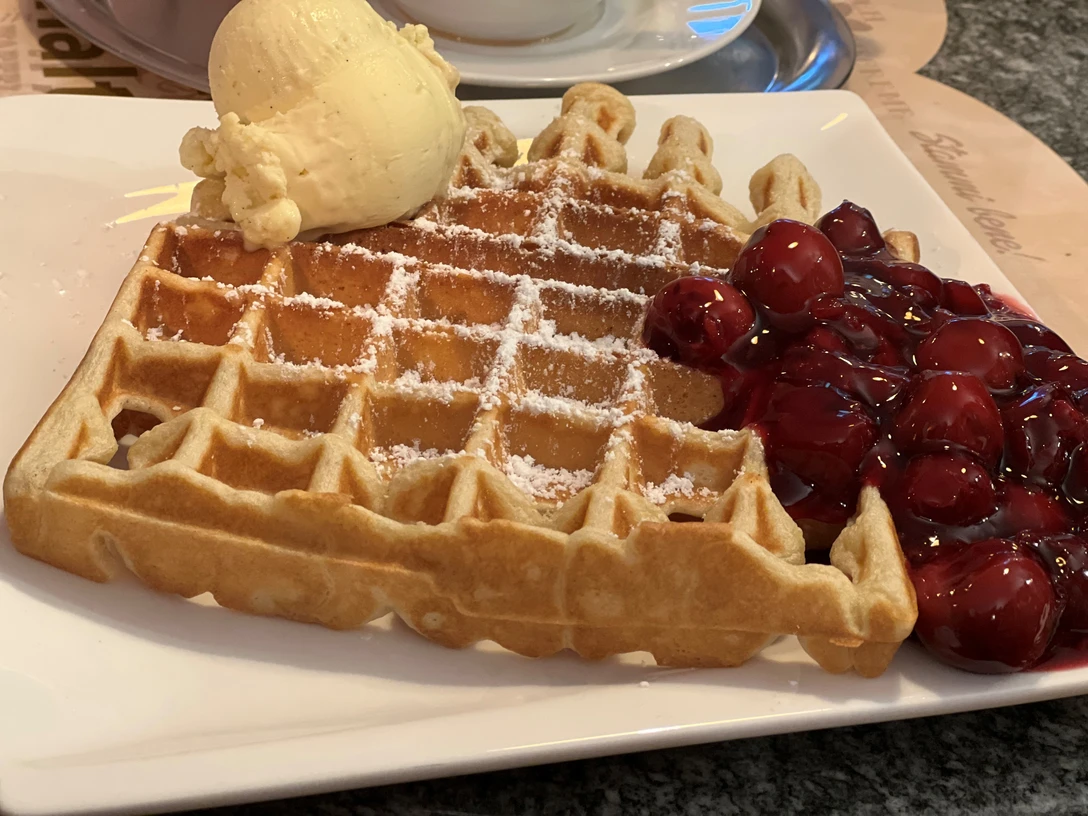 A freshly baked waffle with powdered sugar, cherries and a scoop of vanilla ice cream on a plate.