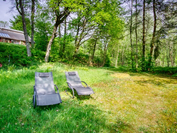 relax-am-see-fewo.jpg Zwei graue Sonnenliegen auf einer grünen Wiese unter Bäumen vor einer Ferienwohnung.