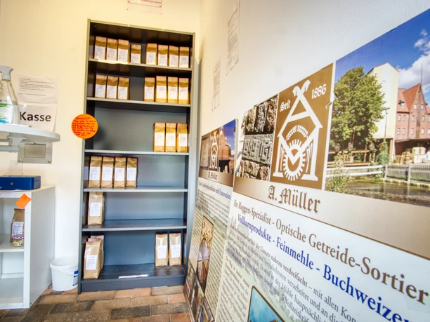 verkaufsraum-3-mühle Regal mit Getreideprodukten und Informationstafeln zur Mühlengeschichte im Hofladen.
