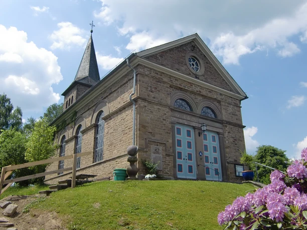 Kirche in der Delling St. Margareta Kirche in Kürten, historisches Gebäude mit Steinfassade, Kirchturm und blühenden Sträuchern.