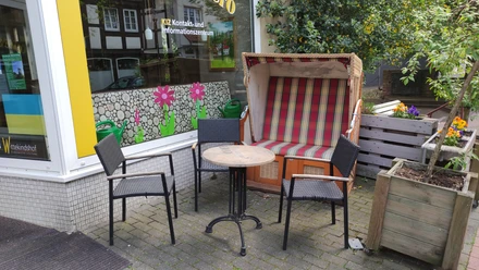 Cafe Solero Vlotho Drei Bistrostühle und ein runder Tisch stehen vor einem rot-weiß gestreiften Strandkorb auf gepflastertem Boden.