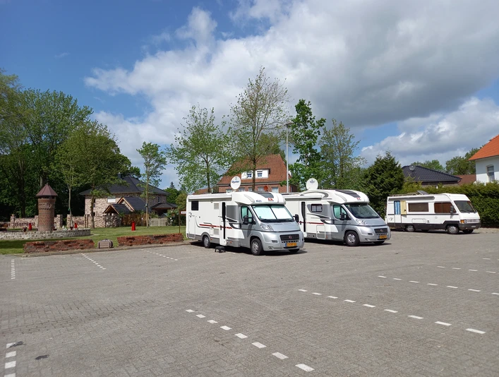 Wohnmobilstellplatz am Viehmarktplatz Der Wohnmobilstellplatz am Viehmarktplatz zeigt drei Wohnmobile, die auf einem gut gepflasterten Parkplatz vor beigefarbenen Steinhäusern mit roten Dächern und üppigen grünen Bäumen stehen. Der blaue Himmel ist leicht bewölkt.