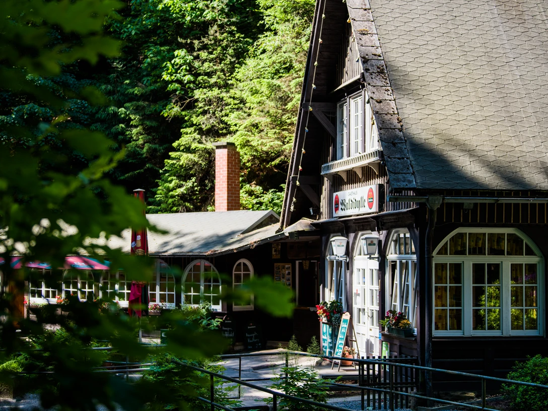 Waldidylle Inn Gemütliches Gasthaus mit Satteldach und weißen Fenstern, umgeben von üppigem Grün und Sonnenschein; einladende Atmosphäre.Cozy inn with gabled roof and white windows, surrounded by lush greenery and sunshine; inviting atmosphere.Útulný hostinec se sedlovou střechou a bílými okny, obklopený bujnou zelení a sluncem; příjemná atmosféra.Przytulny zajazd z dwuspadowym dachem i białymi oknami, otoczony bujną zielenią i słońcem; zachęcająca atmosfera.Gezellige herberg met zadeldak en witte ramen, omgeven door weelderig groen en zonneschijn; uitnodigende sfeer.Accogliente locanda con tetto a capanna e finestre bianche, circondata da una vegetazione lussureggiante e dal sole; atmosfera invitante.