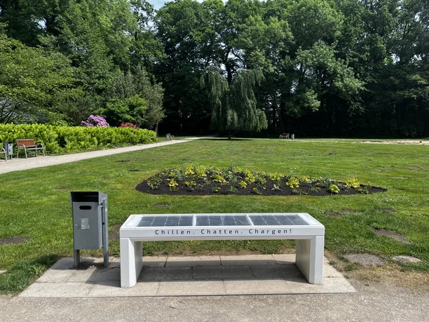 SmartBench mit Solarpanel im Park, umgeben von Blumenbeet, bietet USB-Ladefunktion und WLAN.
