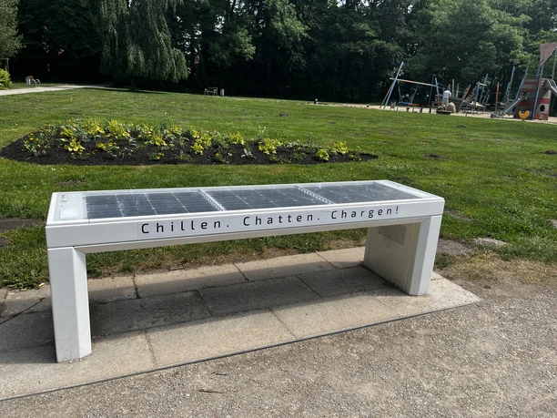 SmartBench mit integriertem Solarpanel in einem grünen Park, ausgestattet mit dabei USB-Ladeanschlüssen.