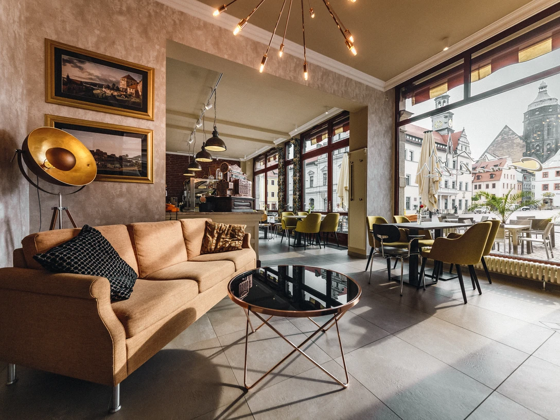 Restaurace Canaletto Gemütliches Café mit beiger Couch, schwarzem Kissen, rundem Glastisch und großen Fenstern mit Blick auf historische Gebäude.Cozy café with beige couch, black cushions, round glass table and large windows with a view of historic buildings.Útulná kavárna s béžovou pohovkou, černými polštáři, kulatým skleněným stolem a velkými okny s výhledem na historické budovy.Przytulna kawiarnia z beżową kanapą, czarnymi poduszkami, okrągłym szklanym stołem i dużymi oknami z widokiem na zabytkowe budynki.Gezellig café met beige bank, zwarte kussens, ronde glazen tafel en grote ramen met uitzicht op historische gebouwen.Accogliente caffè con divano beige, cuscini neri, tavolo rotondo in vetro e grandi finestre con vista sugli edifici storici.