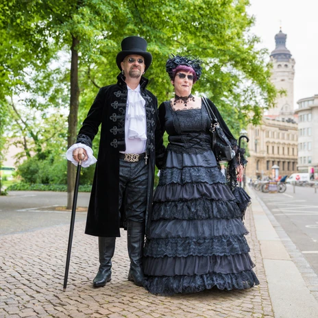 Two people dressed in elaborate black costumes visit the Wave-Gotik-Treffen in Leipzig, in the background the New Town Hall, events, music, culture, scene