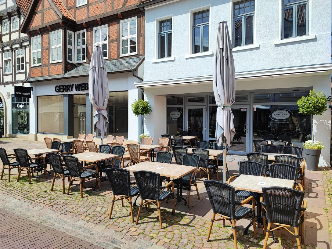 Einladender Außenbereich eines Cafés in einer gepflasterten, sonnigen Fußgängerzone.