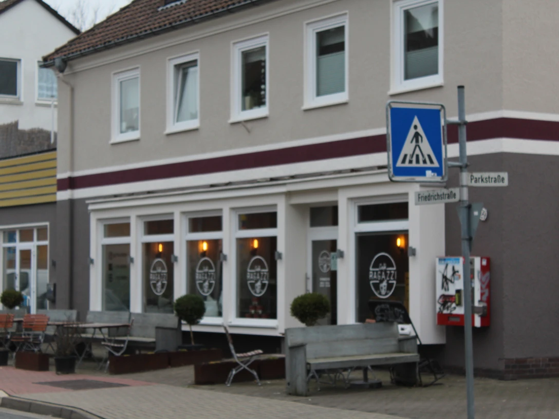 Café mit Fensterfront und Außenterrasse, daneben ein Straßenschild für einen Fußgängerüberweg.