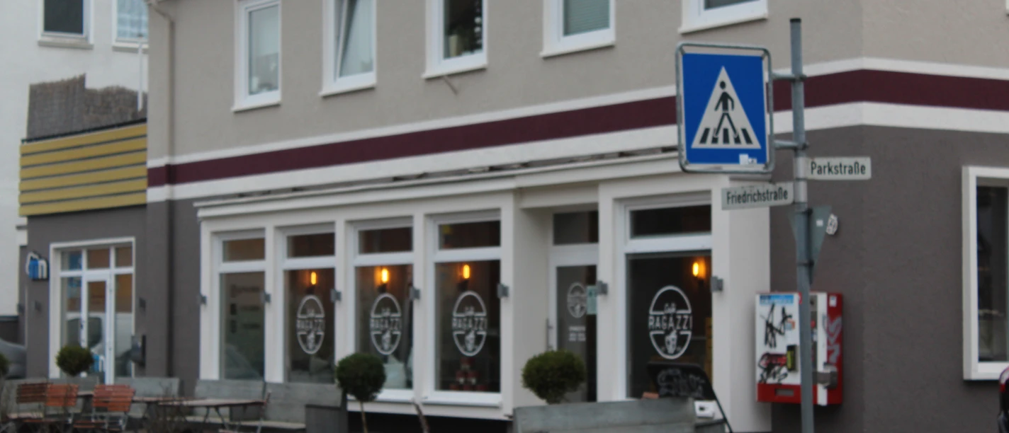 Café with window front and outdoor terrace, next to it a street sign for a crosswalk.