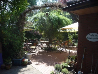 Ein gemütlicher, von Pflanzen umgebener Garten mit Tischen, Stühlen und schattenspendenden Sonnenschirmen.