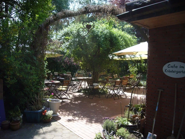 Ein gemütlicher, von Pflanzen umgebener Garten mit Tischen, Stühlen und schattenspendenden Sonnenschirmen.