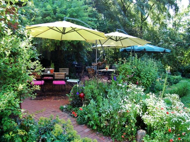 Ein idyllischer Garten mit üppigem Grün, Blumenbeeten und Sitzplätzen unter großen Sonnenschirmen.