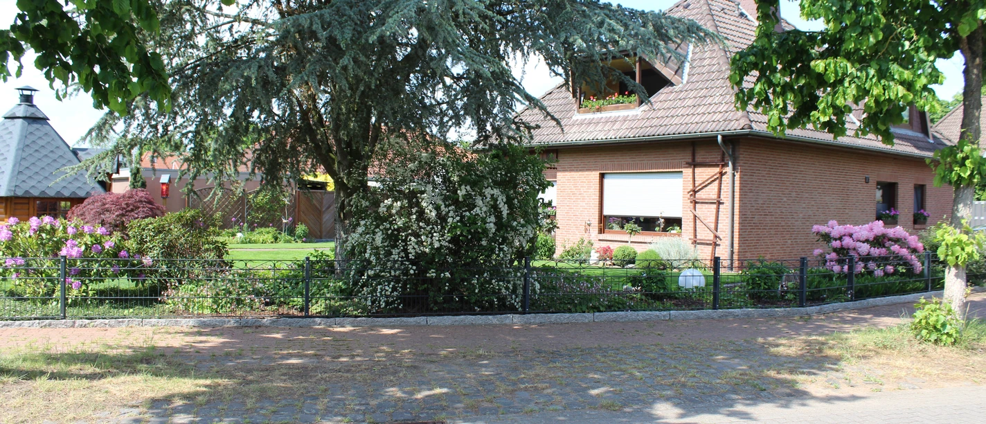 Fam. Jäger Ein rotes Backsteinhaus mit gepflegtem Garten und blühenden Sträuchern; ein einladender Ort.