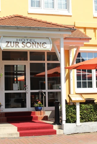 Der Eingang des Hotels zur Sonne mit rotem Teppich, orangenen Sonnenschirmen und Topfpflanzen.The entrance to the Hotel zur Sonne with its red carpet, orange parasols and potted plants.Indgangen til Hotel zur Sonne med sit røde tæppe, orange parasoller og potteplanter.De ingang van Hotel zur Sonne met zijn rode tapijt, oranje parasols en potplanten.