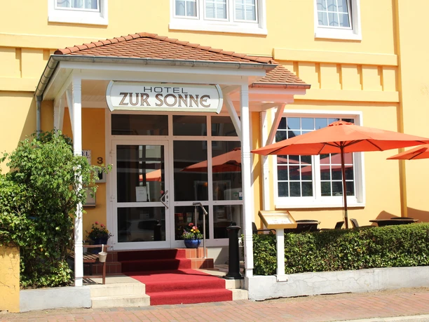 De ingang van Hotel zur Sonne met zijn rode tapijt, oranje parasols en potplanten.