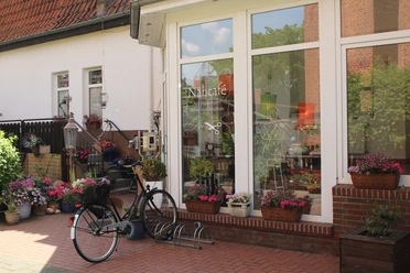 Uitnodigend naaicafé met bloeiende bloemen en een fiets voor grote, uitnodigende ramen.