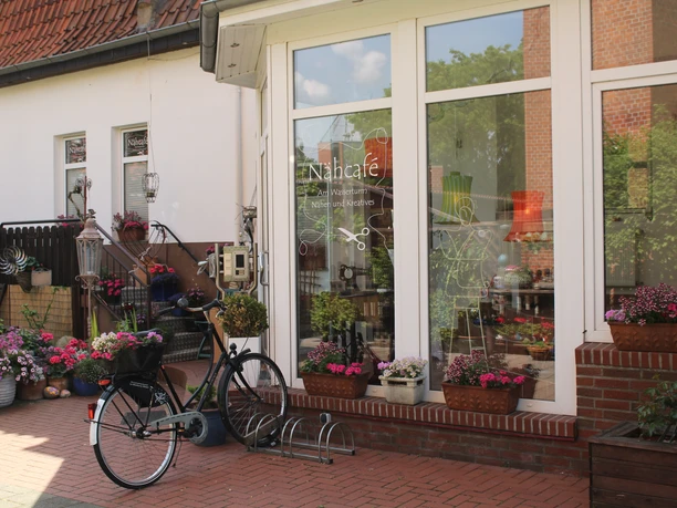 Inviting sewing café with blooming flowers and a bicycle in front of large, inviting windows.