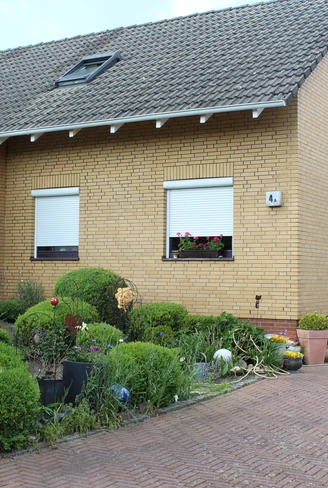 Ein schlichtes Einfamilienhaus aus gelbem Klinker mit Dachfenster, Vorplatz und gepflegtem Vorgarten.